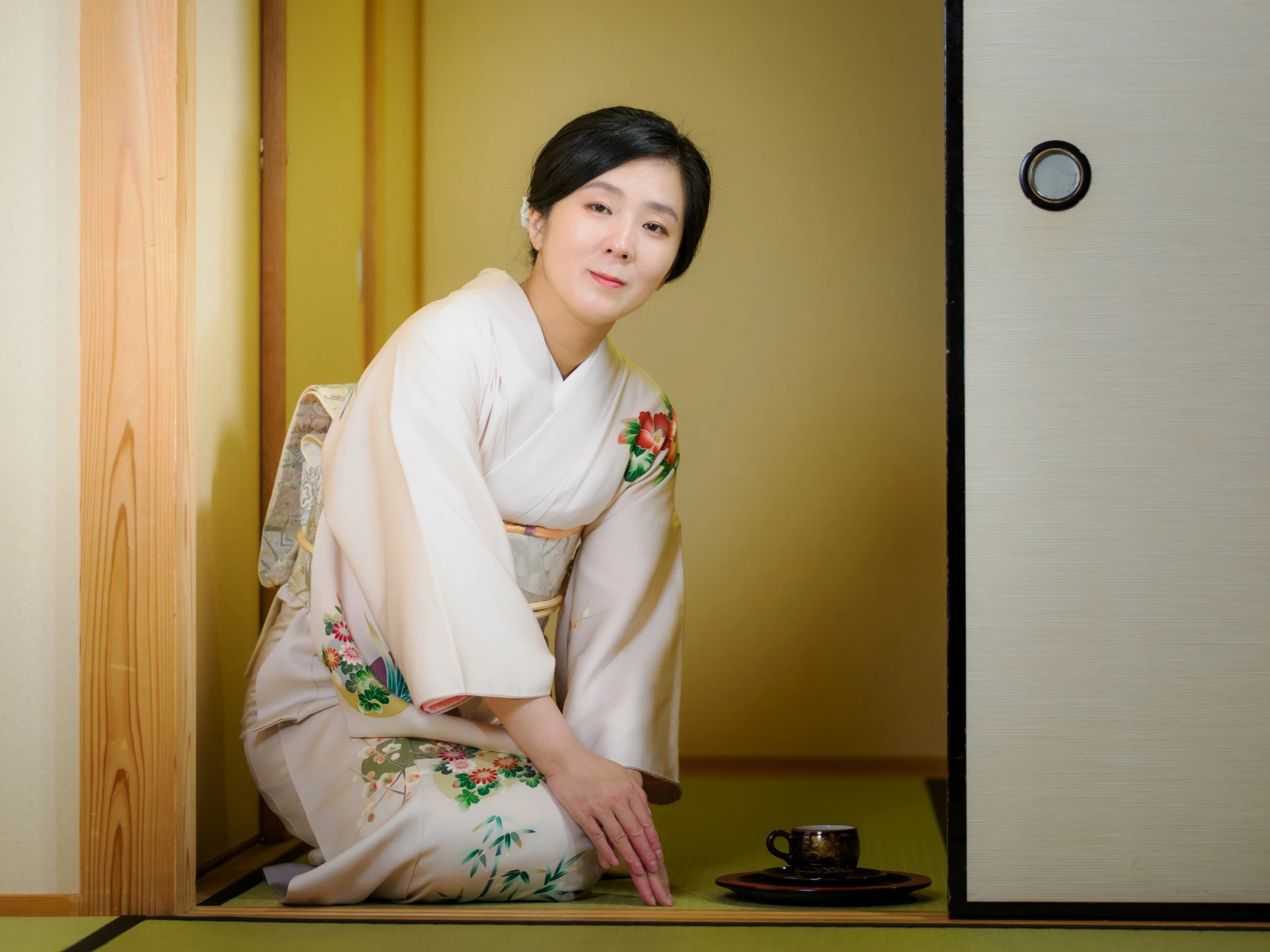 Woman in an elegant kimono, seated in a tatami room, serving tea on a tray.