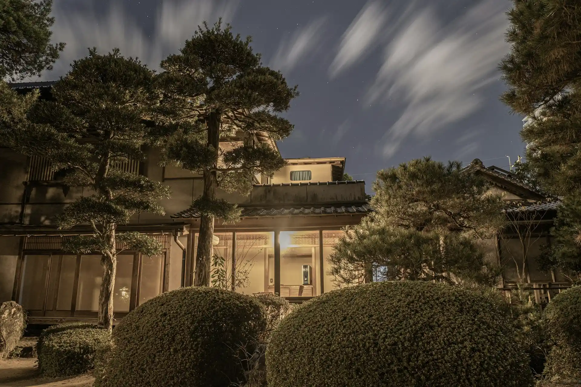 Nighttime view of a traditional Japanese ryokan surrounded by manicured trees and illuminated by soft lights.