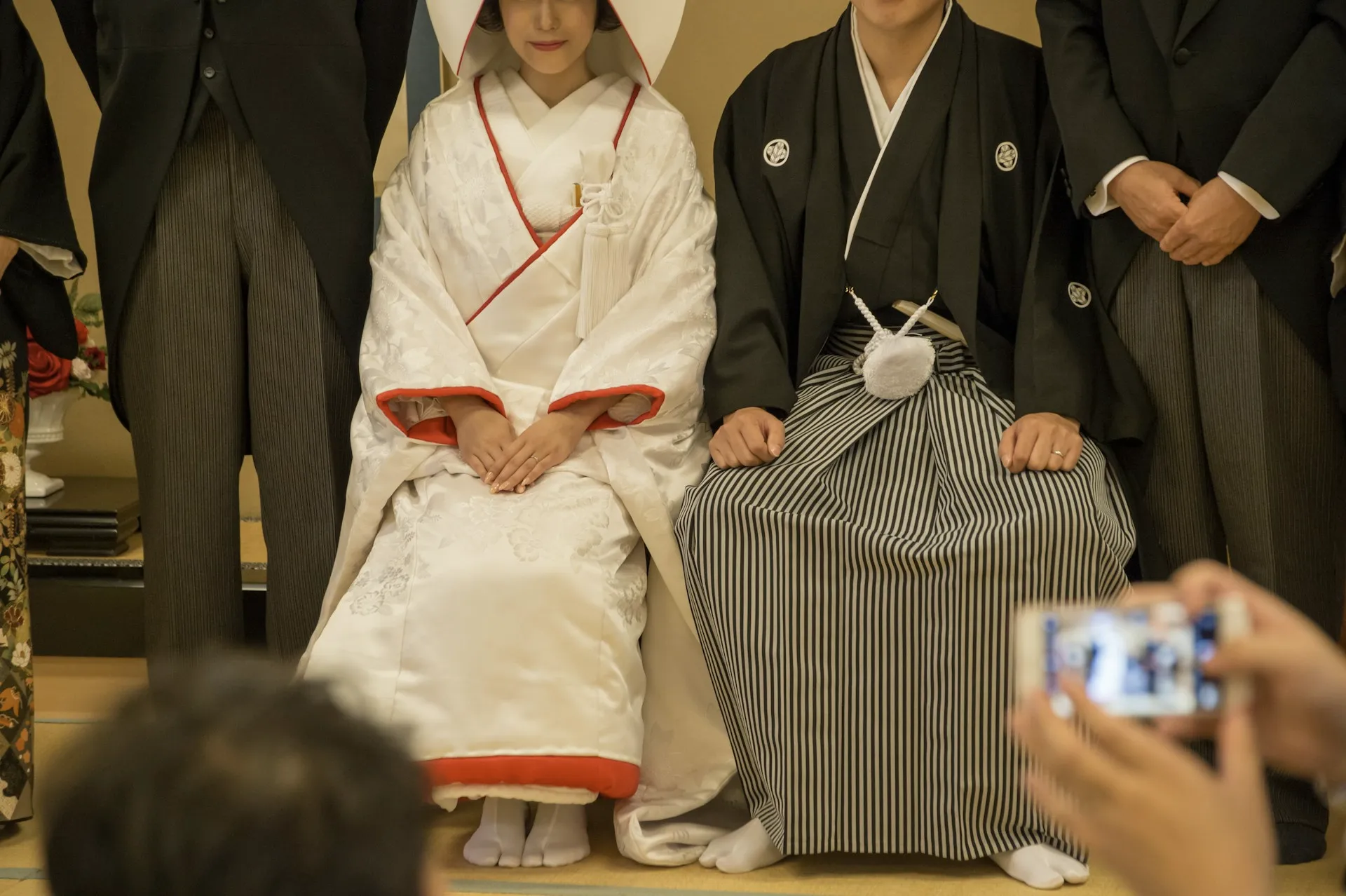 Close-up of bride and groom in traditional Japanese wedding attire seated side by side indoors.