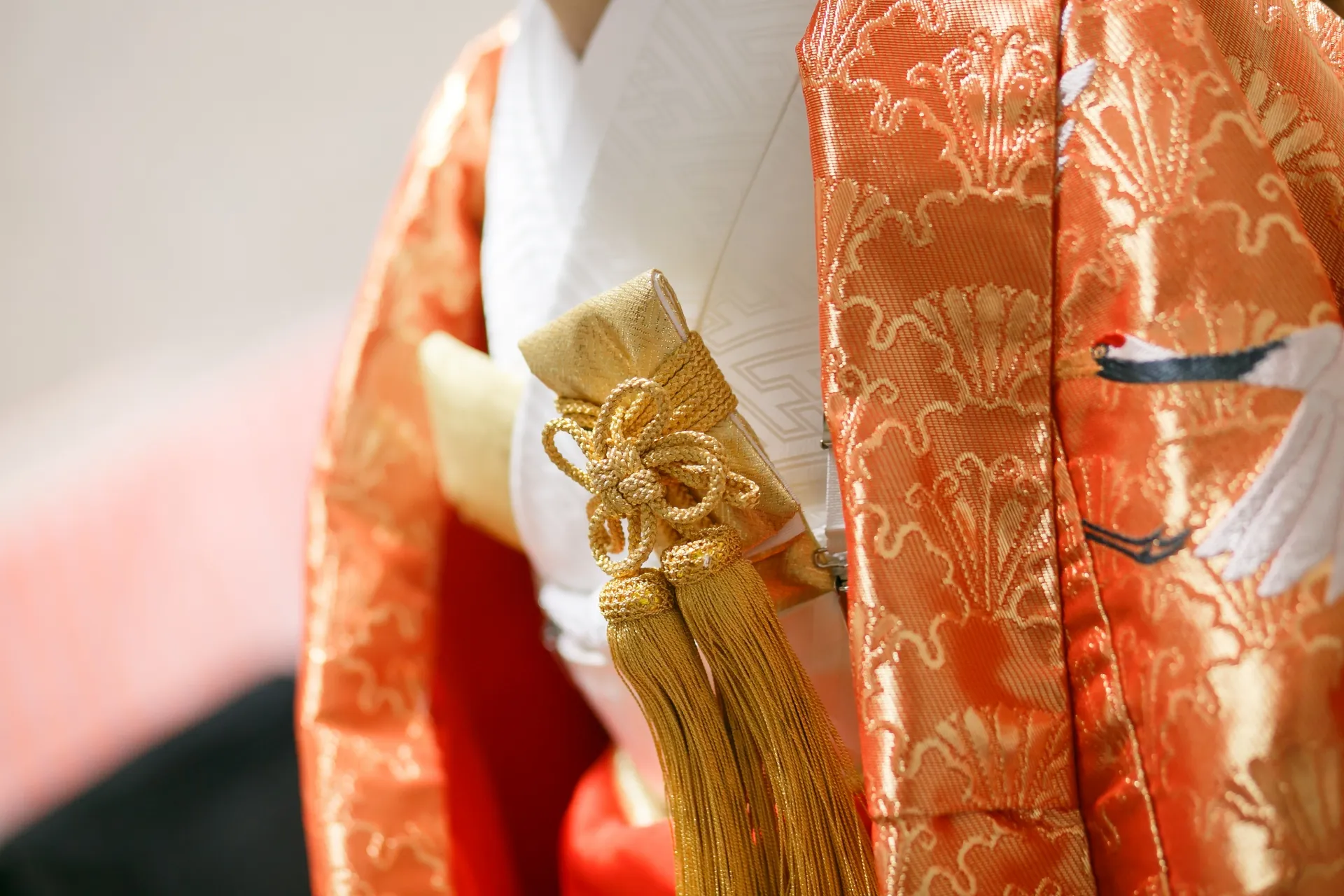 Close-up of a vibrant orange iro uchikake with gold tassel and crane embroidery