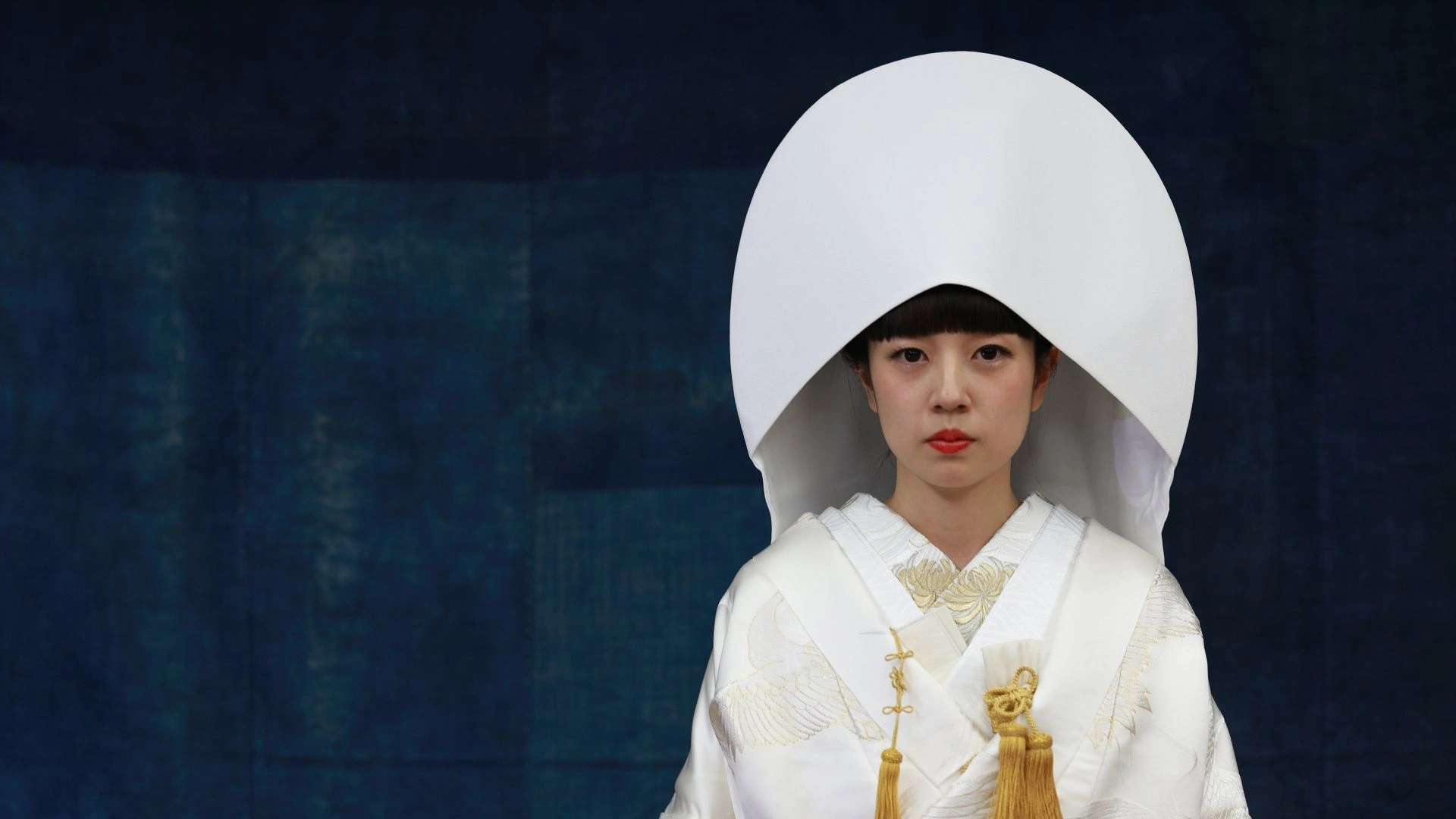 Japanese bride wearing traditional white shiromuku wedding kimono and large white tsunokakushi headpiece, formal portrait against dark background