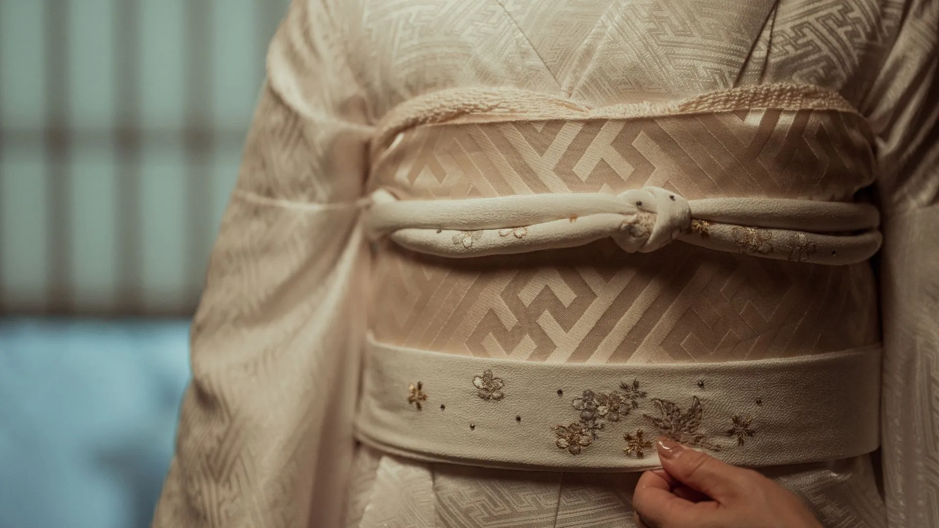 Close-up detail of traditional Japanese shiromuku wedding kimono showing white obi sash, embroidered obijime cord, and intricate gold floral patterns